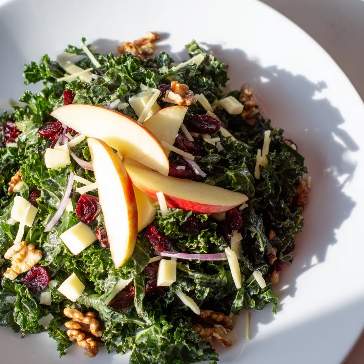 Freshly assembled Winter Kale Salad with apple slices, cheese, and a light, flavorful dressing.