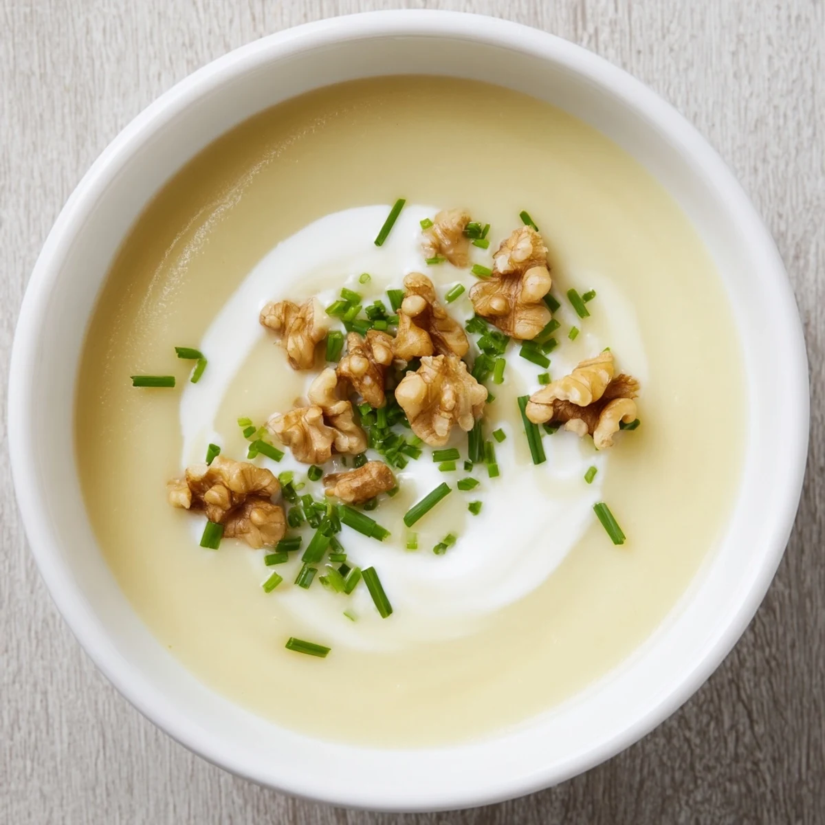 Creamy Parsnip and Pear Soup with Walnuts in a white bowl, garnished with fresh chives and crunchy toasted walnuts.