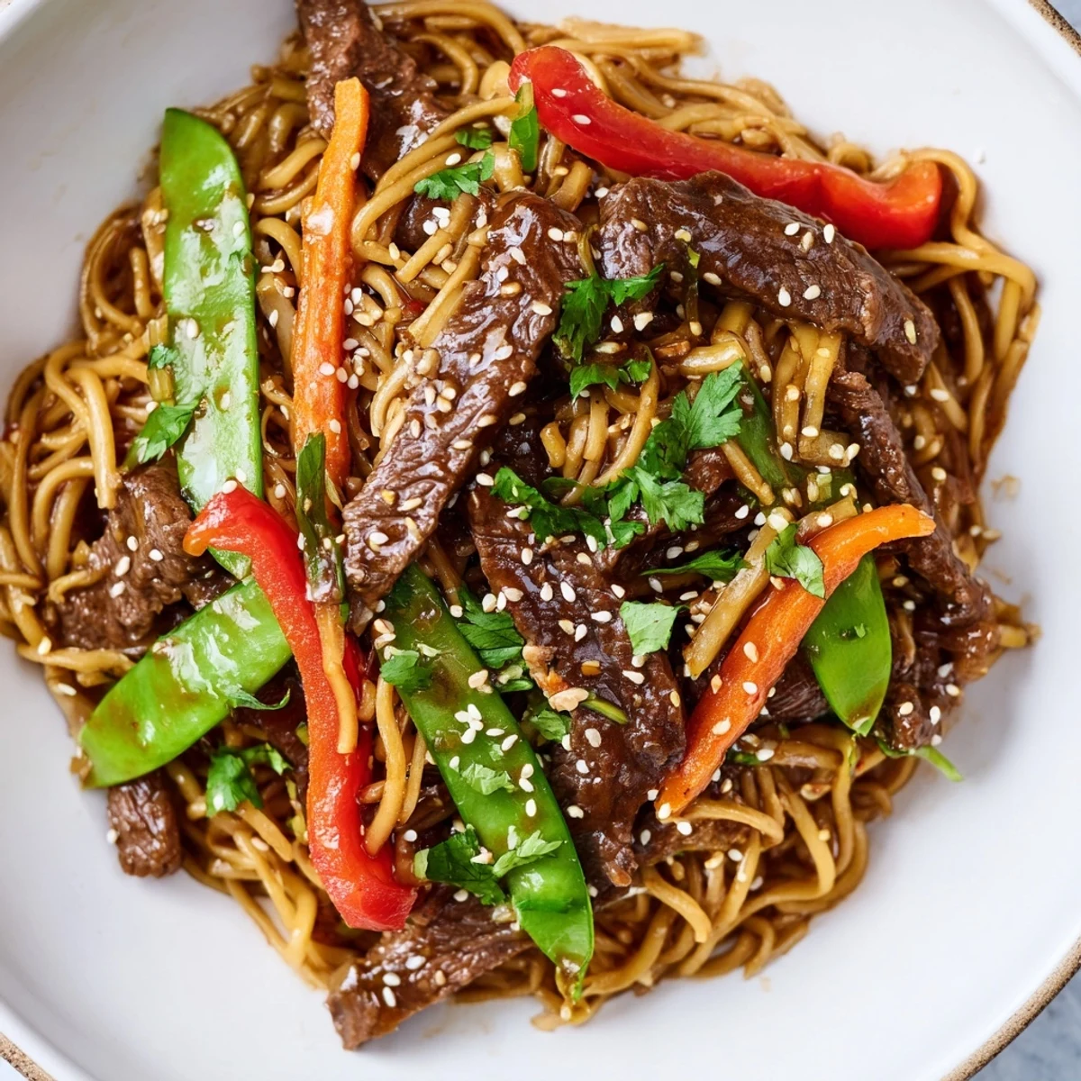 Steaming bowl of Spicy Beef Noodles tossed with tender beef strips, red bell peppers, and fresh garnishes.