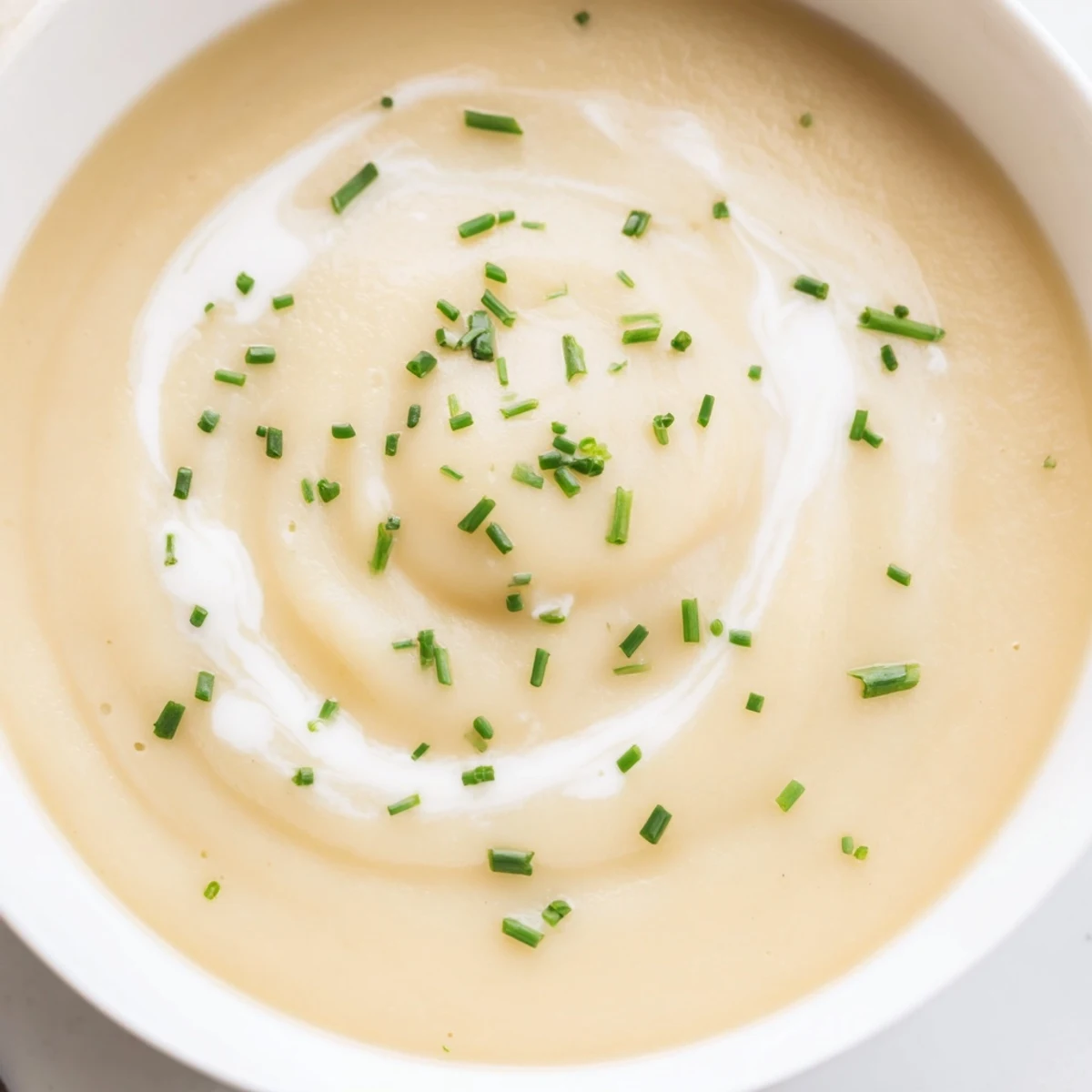 Creamy roasted parsnip and garlic soup topped with herbs, served alongside crusty bread on a wooden table.