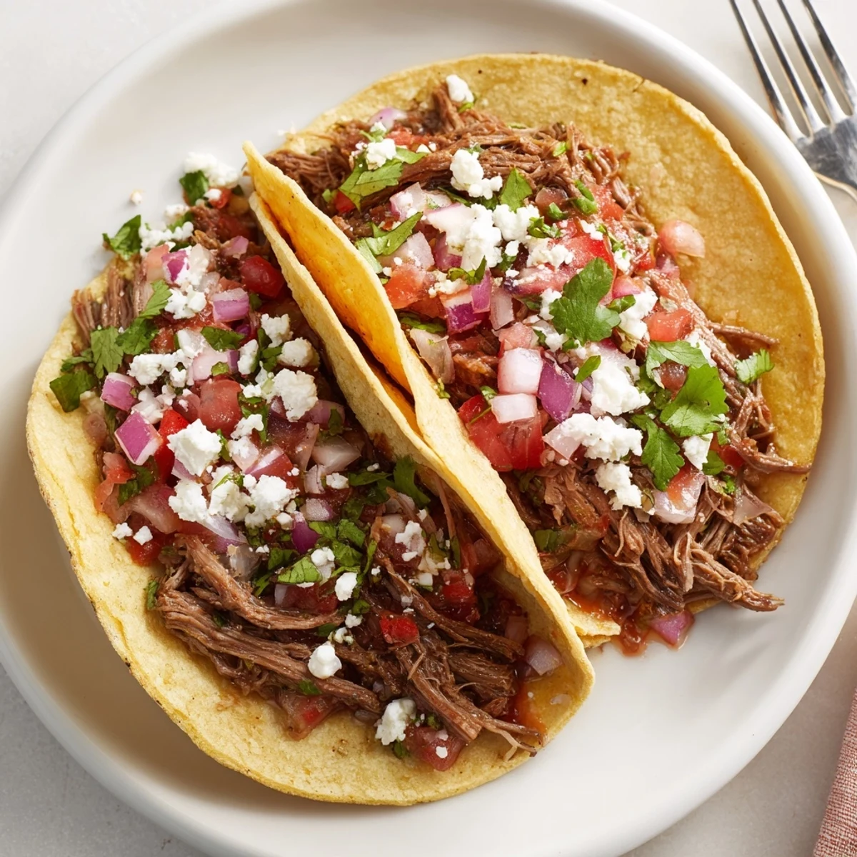 Slow-cooked shredded beef tacos with lime, piled high in warm tortillas topped with fresh cilantro and diced onion for a delicious Mexican-inspired meal.  