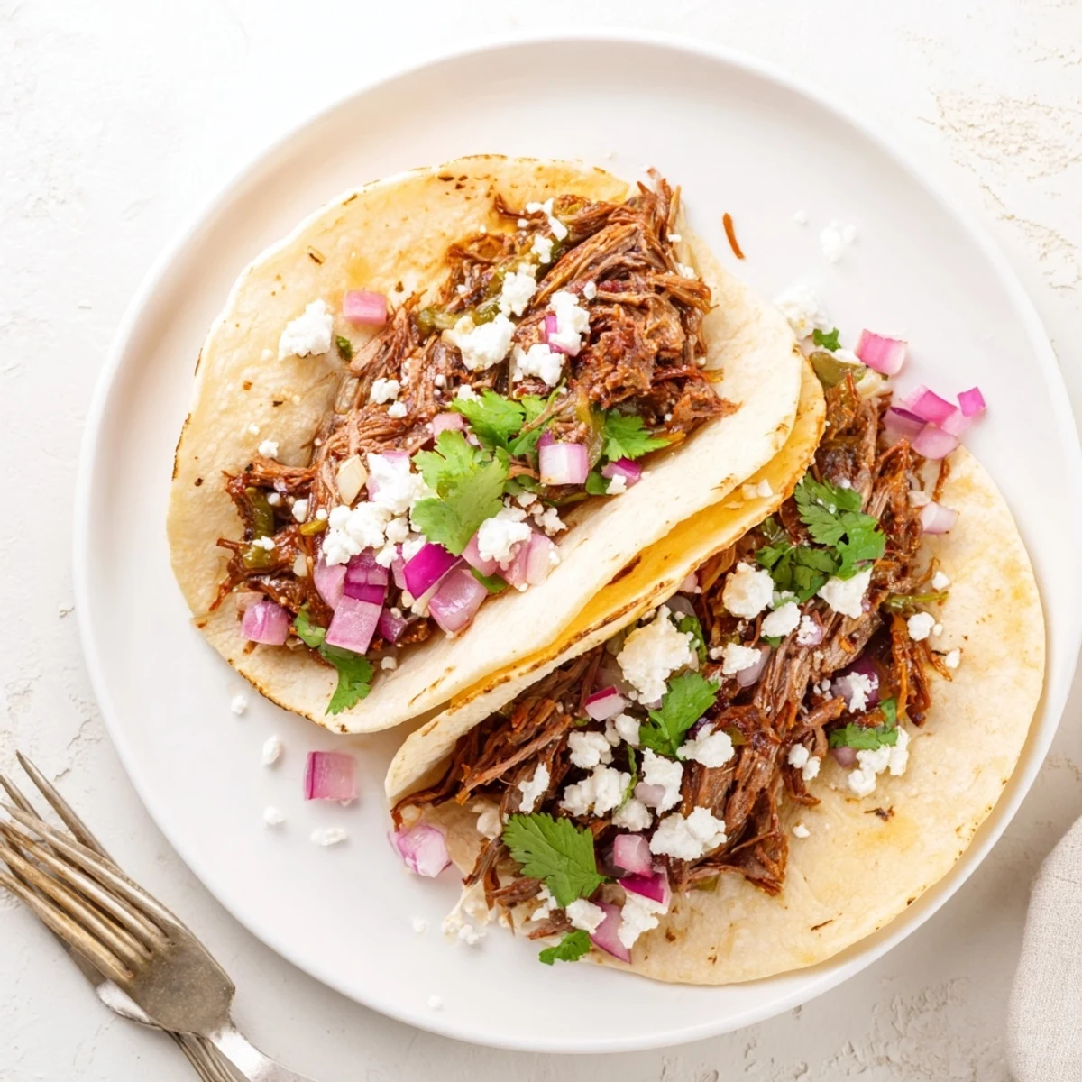 Tender shredded beef tacos with lime, garnished with cilantro and avocado, served on a wooden board ready for a festive taco night.  