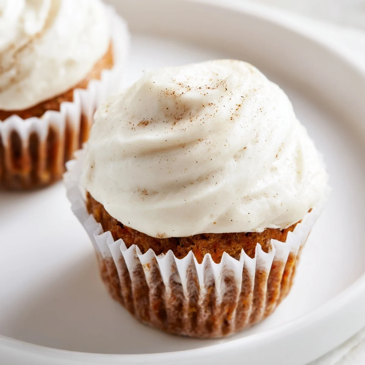 Decadent carrot cake cupcakes with cream cheese frosting, displayed on a rustic wooden board with a fork and vintage tea towel.