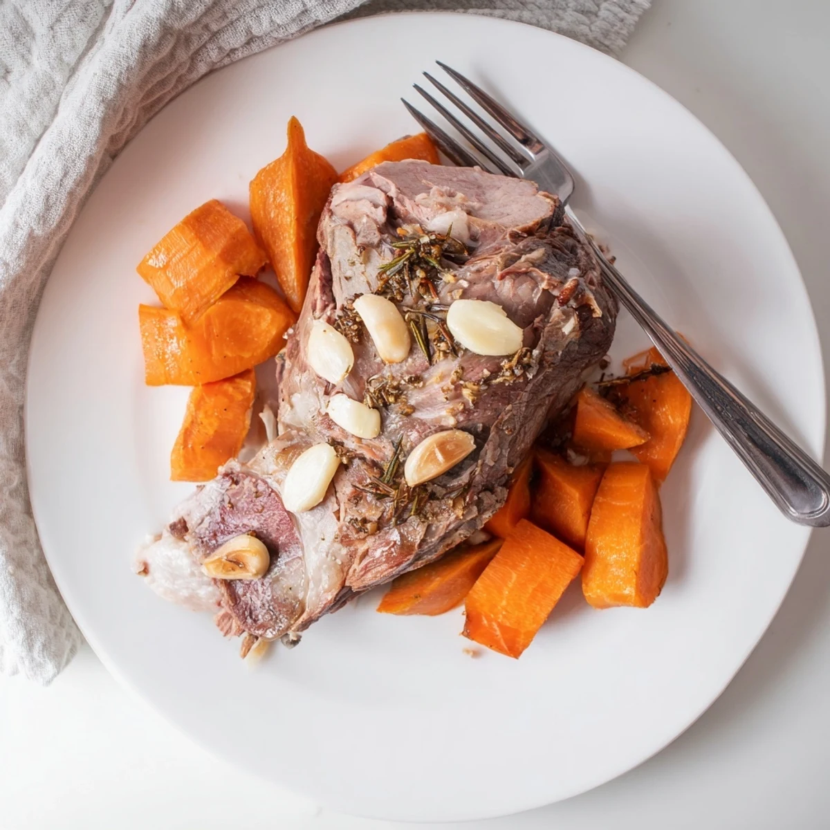 A beautifully plated Slow Roasted Leg of Lamb with Garlic and Lemon, garnished with fresh herbs beside roasted carrots and onions on a rustic table.
