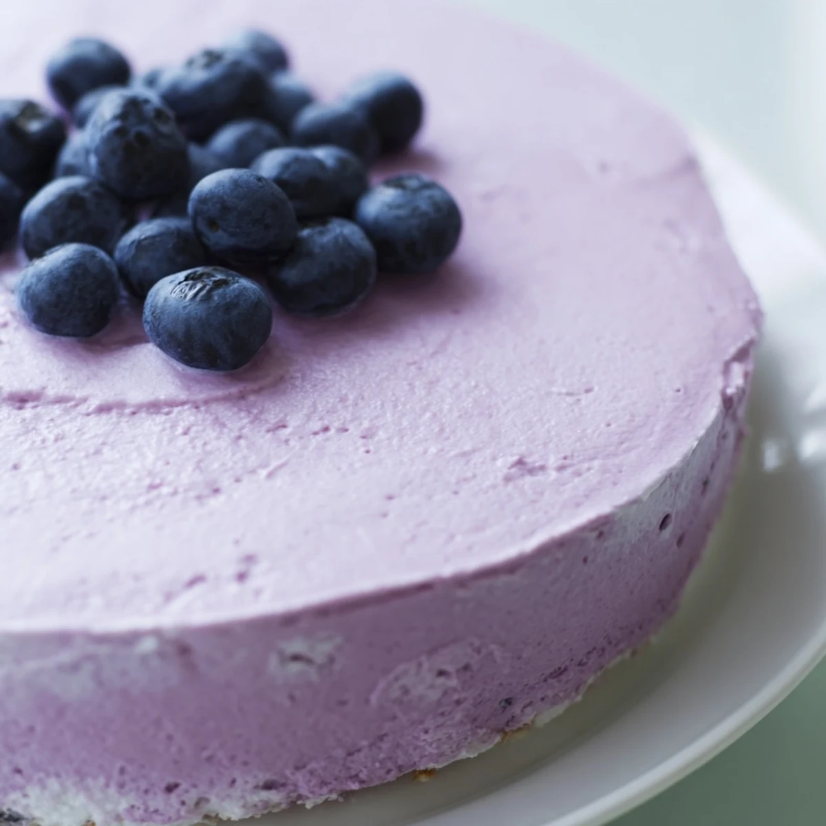 Fresh Blueberry Mousse Cheesecake topped with juicy berries and mint on a marble surface.