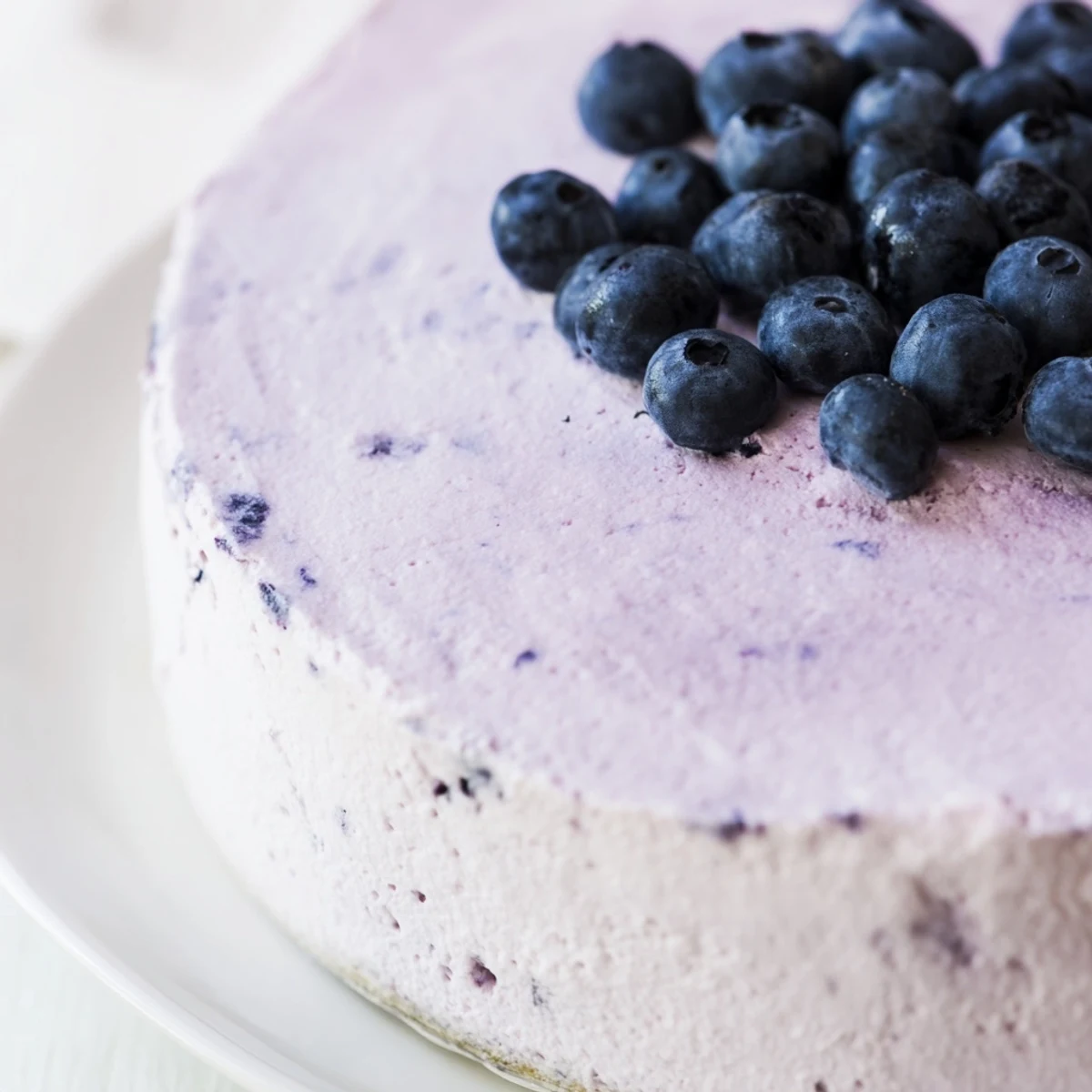 Slice of creamy Blueberry Mousse Cheesecake served on a white plate with whipped cream.
