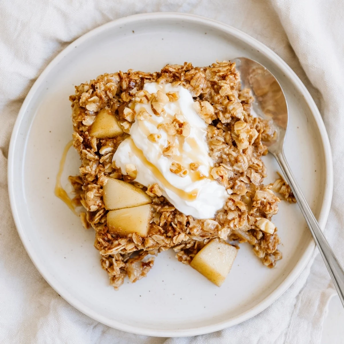 A comforting serving of Baked Apple Oatmeal With Greek Yogurt, finished with a sweet maple drizzle and warm cinnamon aroma.