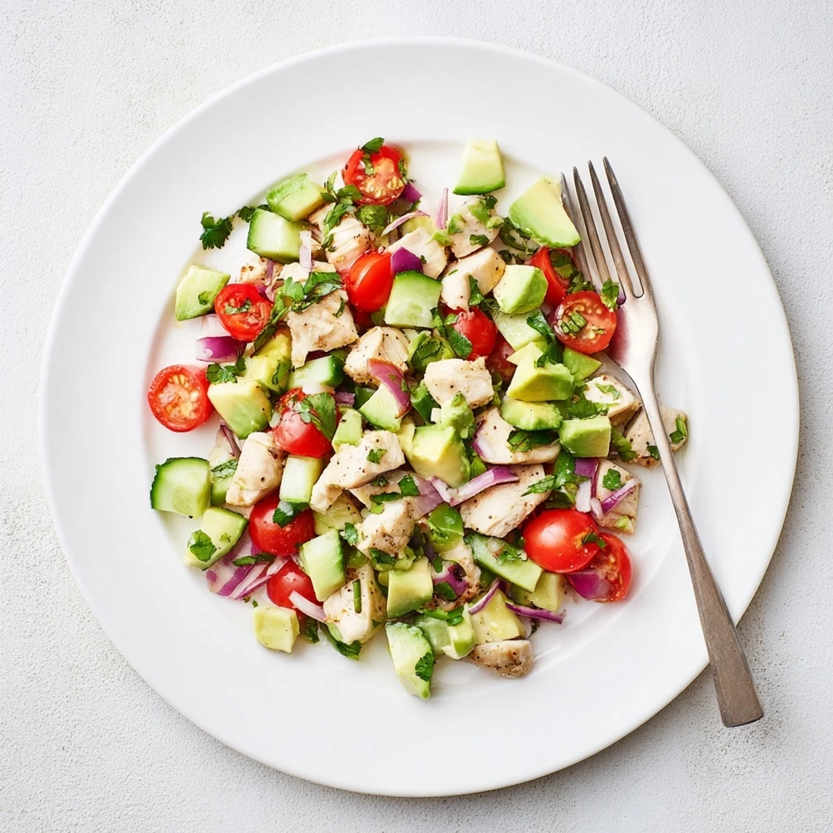 Creamy avocado chicken salad with grilled chicken, cherry tomatoes, and fresh cilantro on a rustic plate.