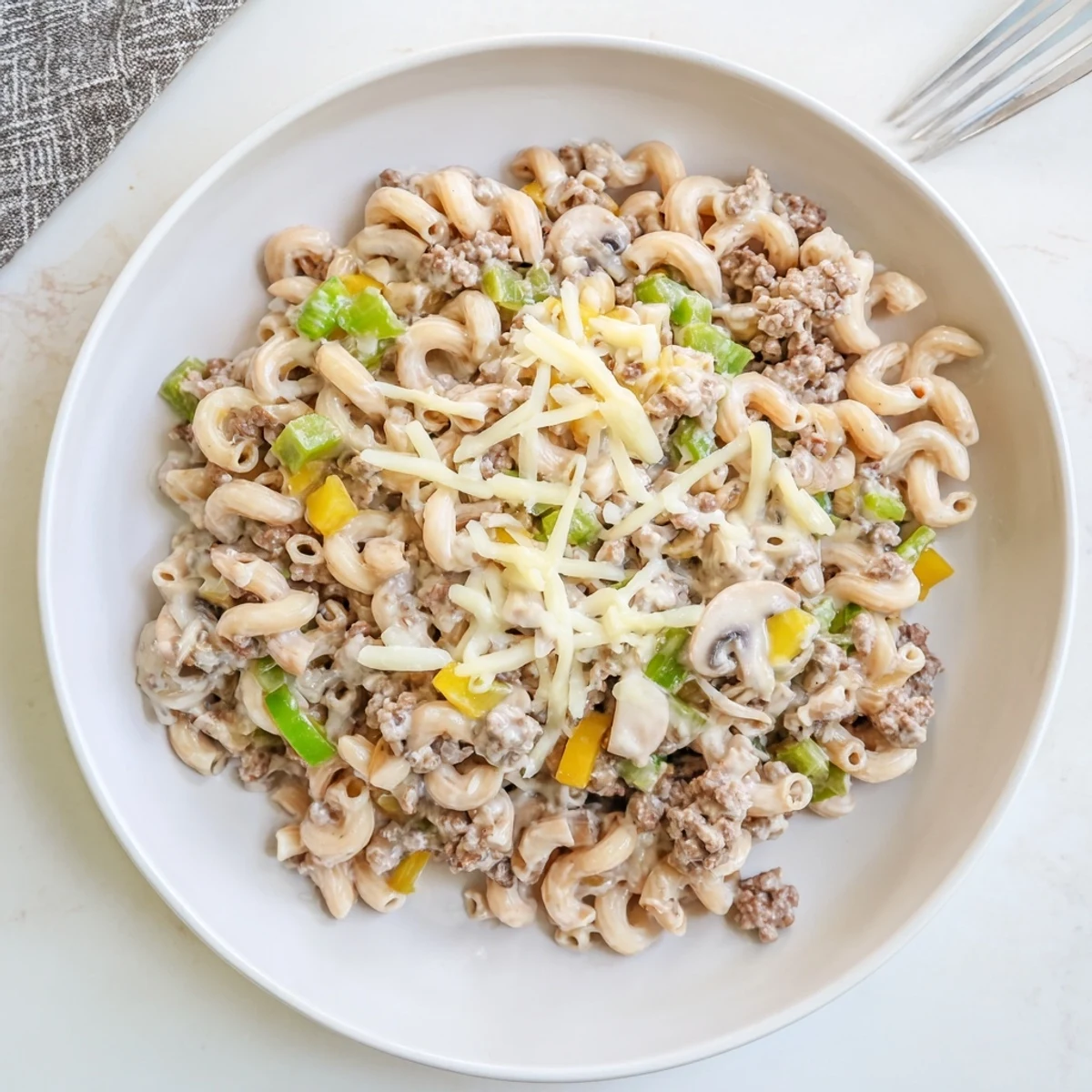 A steaming skillet of Easy High Protein Philly Cheesesteak Mac topped with melted provolone and mozzarella.
