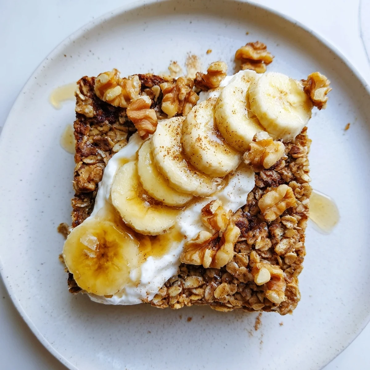 Freshly baked Banana Baked Oatmeal topped with creamy Greek yogurt and sliced bananas on a rustic table. 