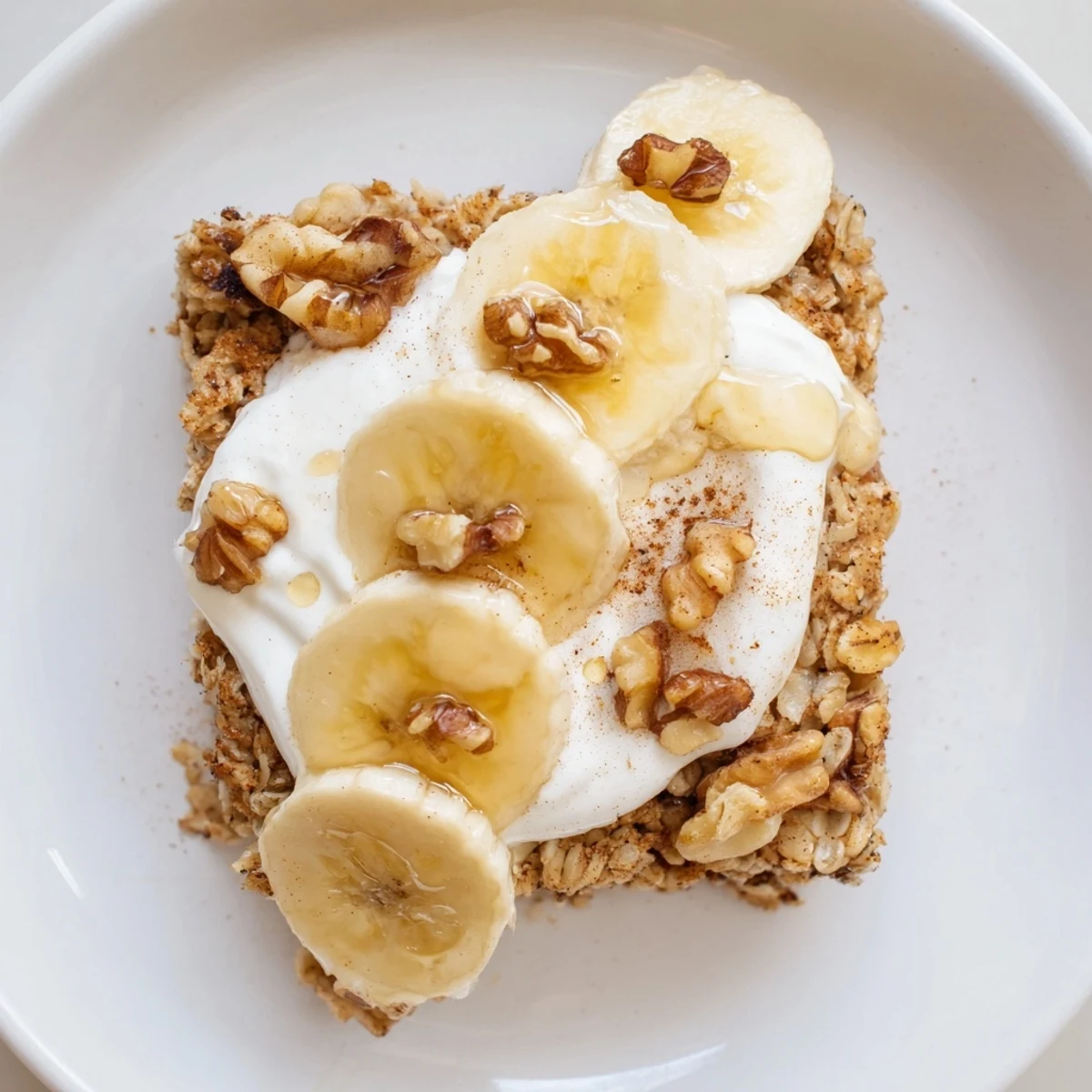 Golden brown Banana Baked Oatmeal in a baking dish, sprinkled with walnuts and a dollop of Greek yogurt.