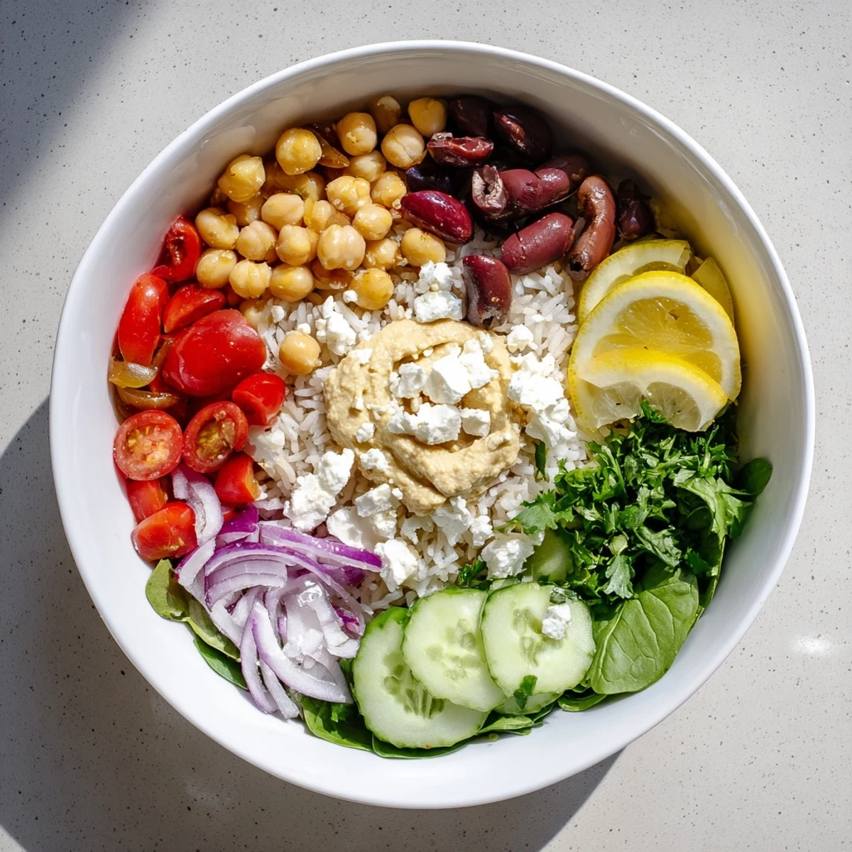 Colorful Mediterranean rice bowl topped with fresh vegetables, hummus, and zesty lemon-tahini drizzle