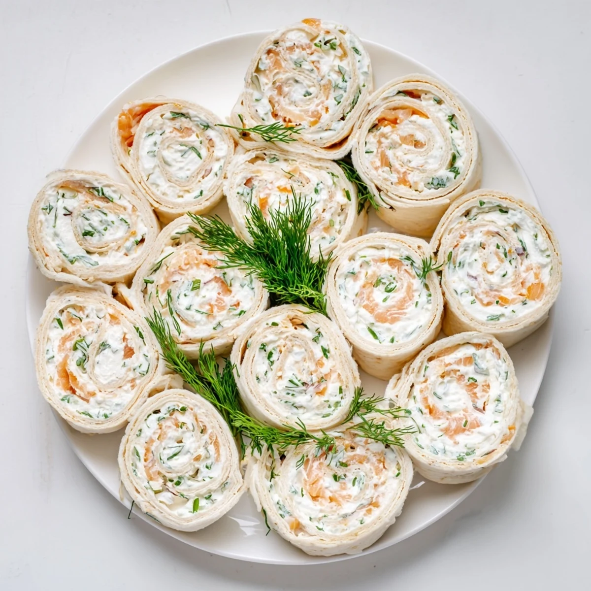 Appetizing smoked salmon roll ups spirals featuring creamy herb cheese filling on white serving platter