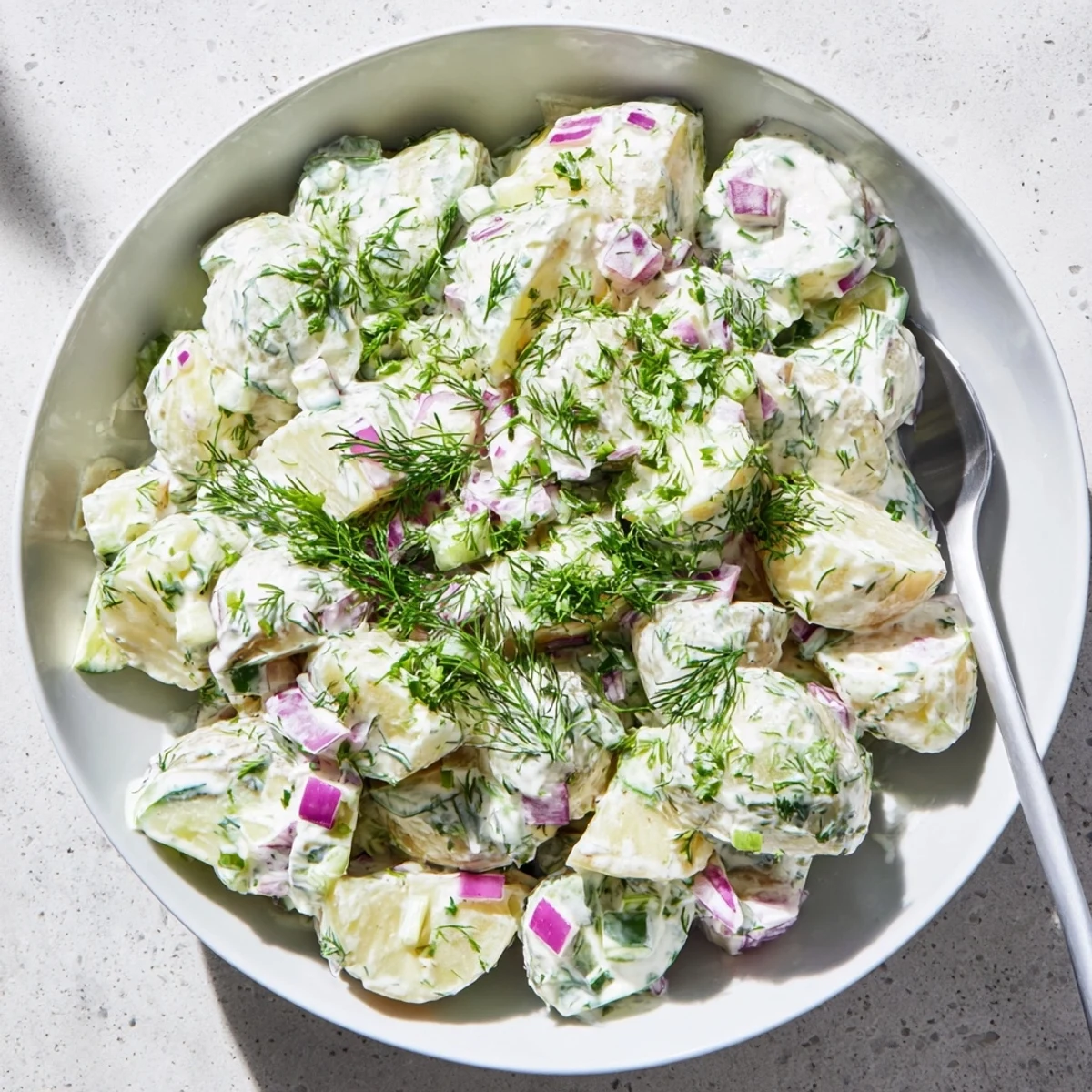 Creamy Greek yogurt potato salad with tender red potatoes, crisp celery, and fresh green herbs in a white serving bowl