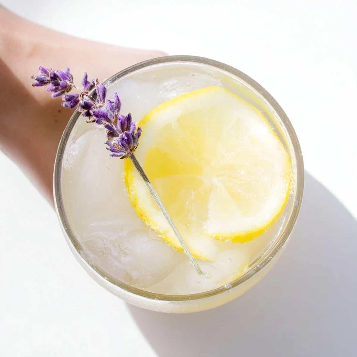 Glass pitcher of lavender lemonade garnished with fresh lemon slices and purple sprigs on a sunny wooden table