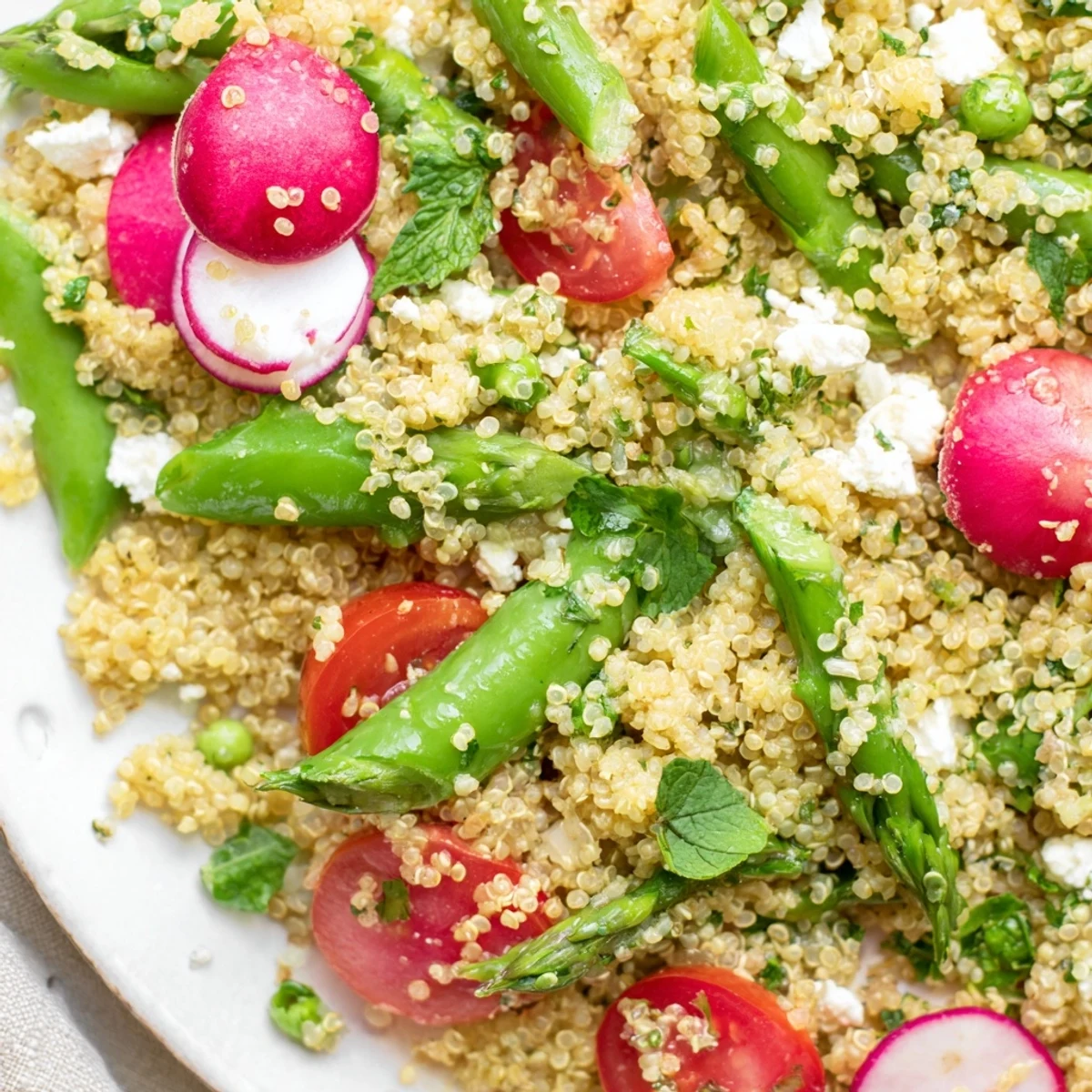 Colorful spring vegetable quinoa salad topped with crumbled feta and bright green asparagus