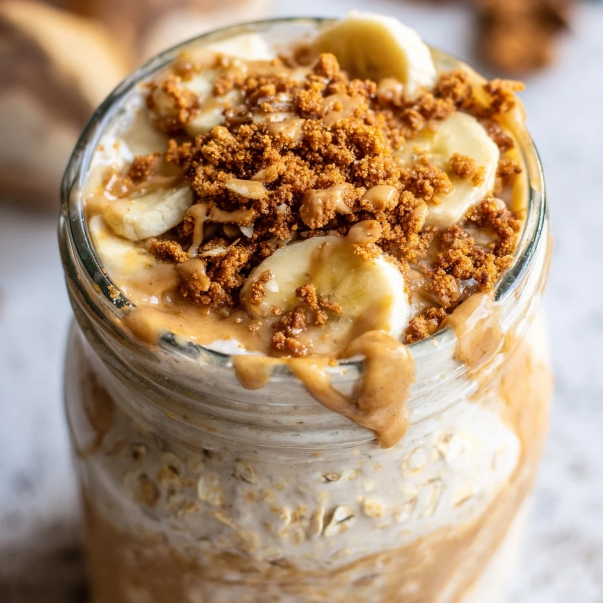 Creamy Biscoff overnight oats topped with crushed cookie pieces and caramel drizzle in glass jar