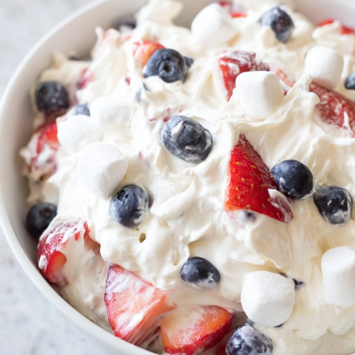 Creamy Red White Blue Cheesecake Salad topped with fresh strawberries and blueberries in a white bowl