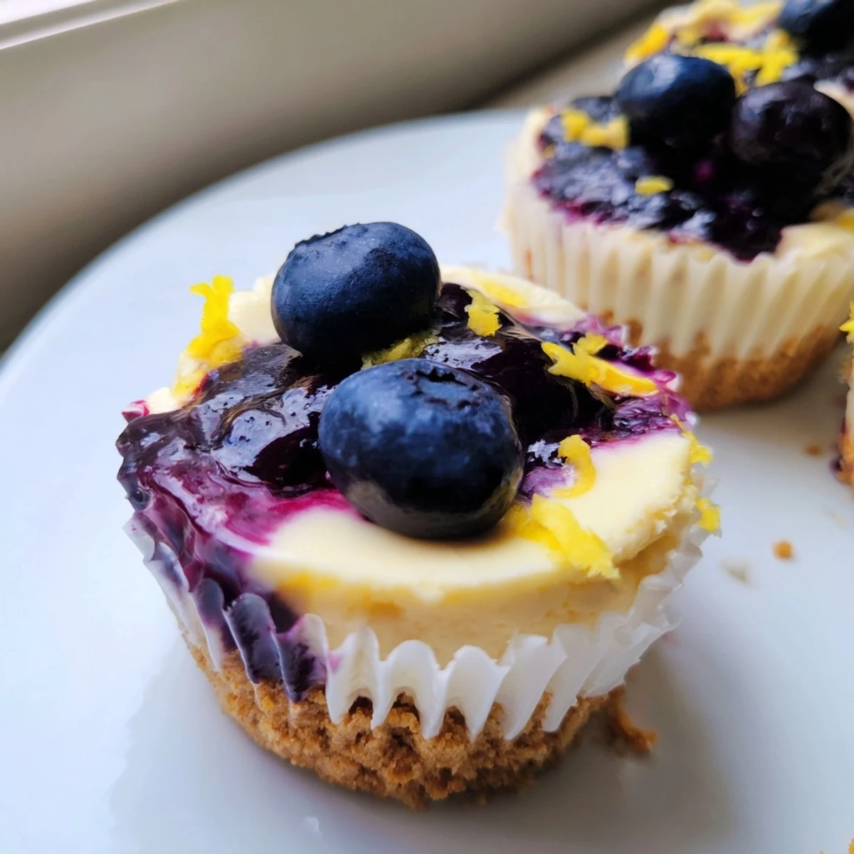 Golden graham cracker crusts cradle creamy Mini Lemon Blueberry Cheesecakes swirled with purple fruit