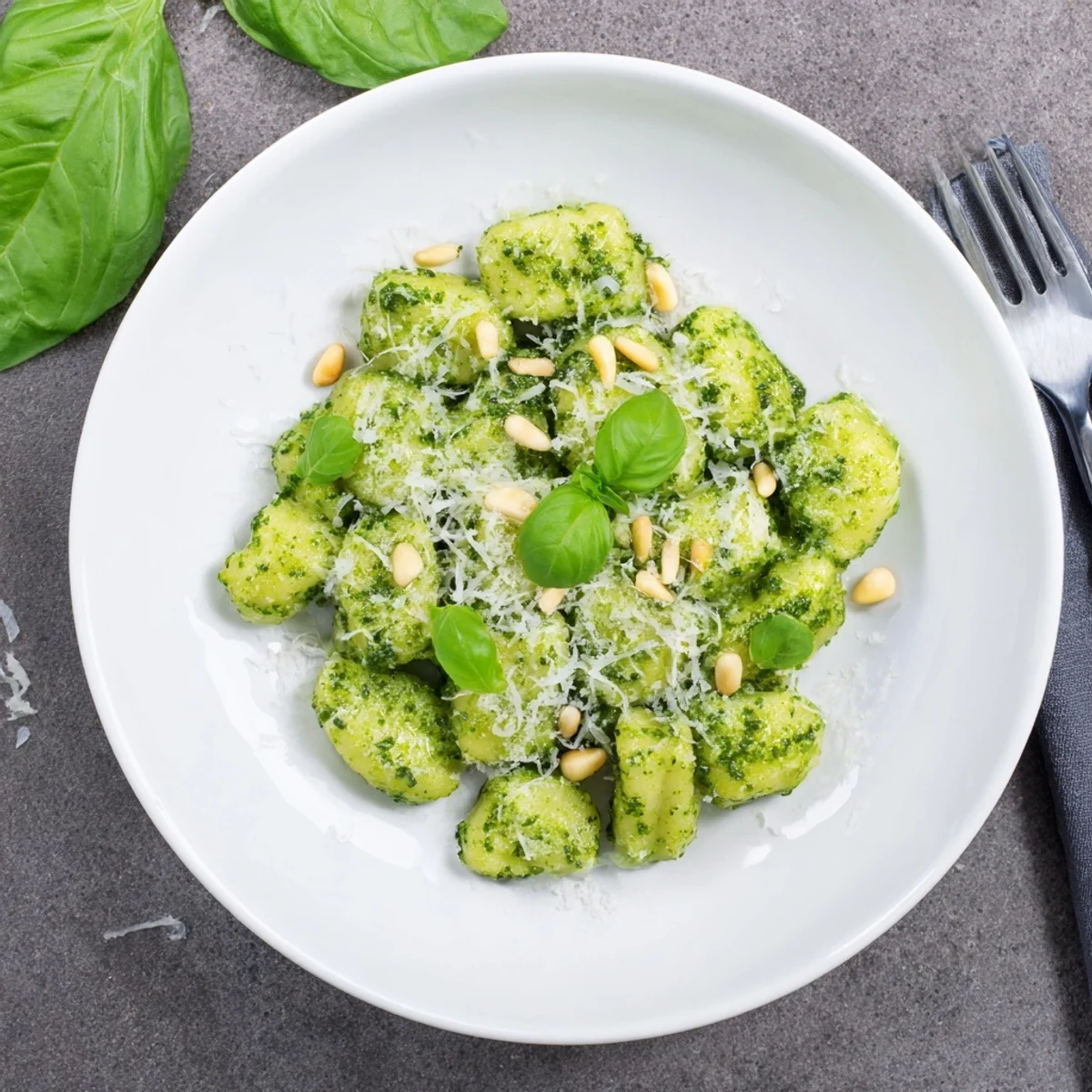 Italian pesto gnocchi plated with extra cheese, basil garnish, and pine nuts