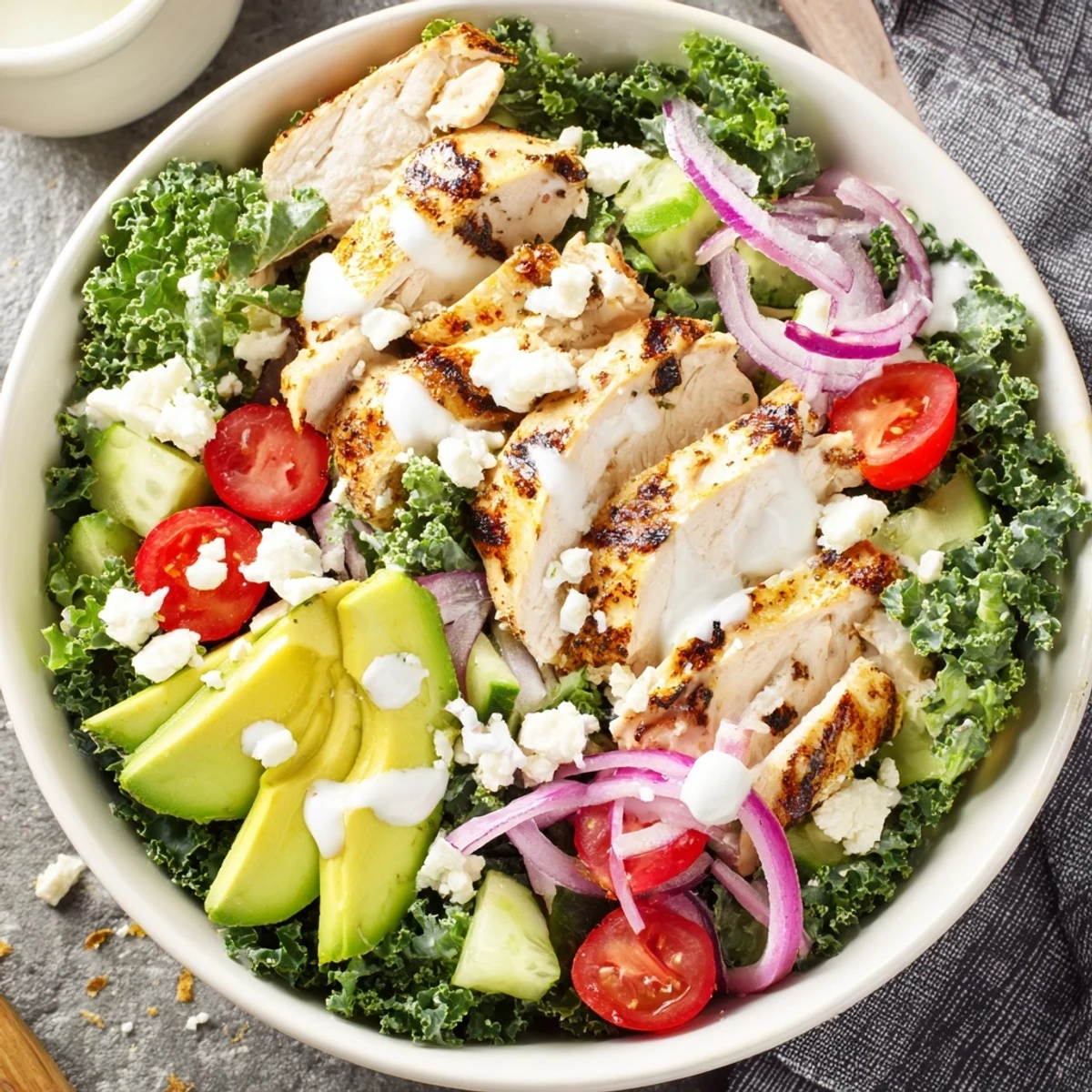 Colorful marinated kale and chicken bowl with fresh vegetables, sliced avocado, and zesty yogurt dressing