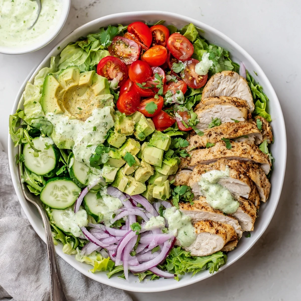 Colorful creamy avocado grilled chicken salad bowl with sliced juicy chicken breast over fresh mixed greens, tomatoes, and cucumber