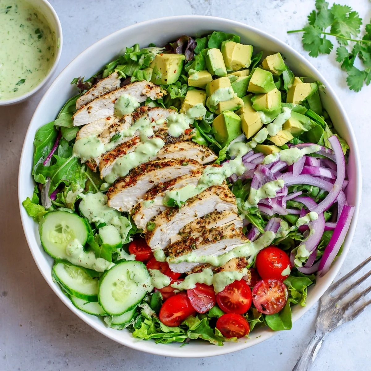 Protein-packed grilled chicken salad bowl with creamy avocado pieces, colorful cherry tomatoes, red onion, and vibrant cilantro garnish