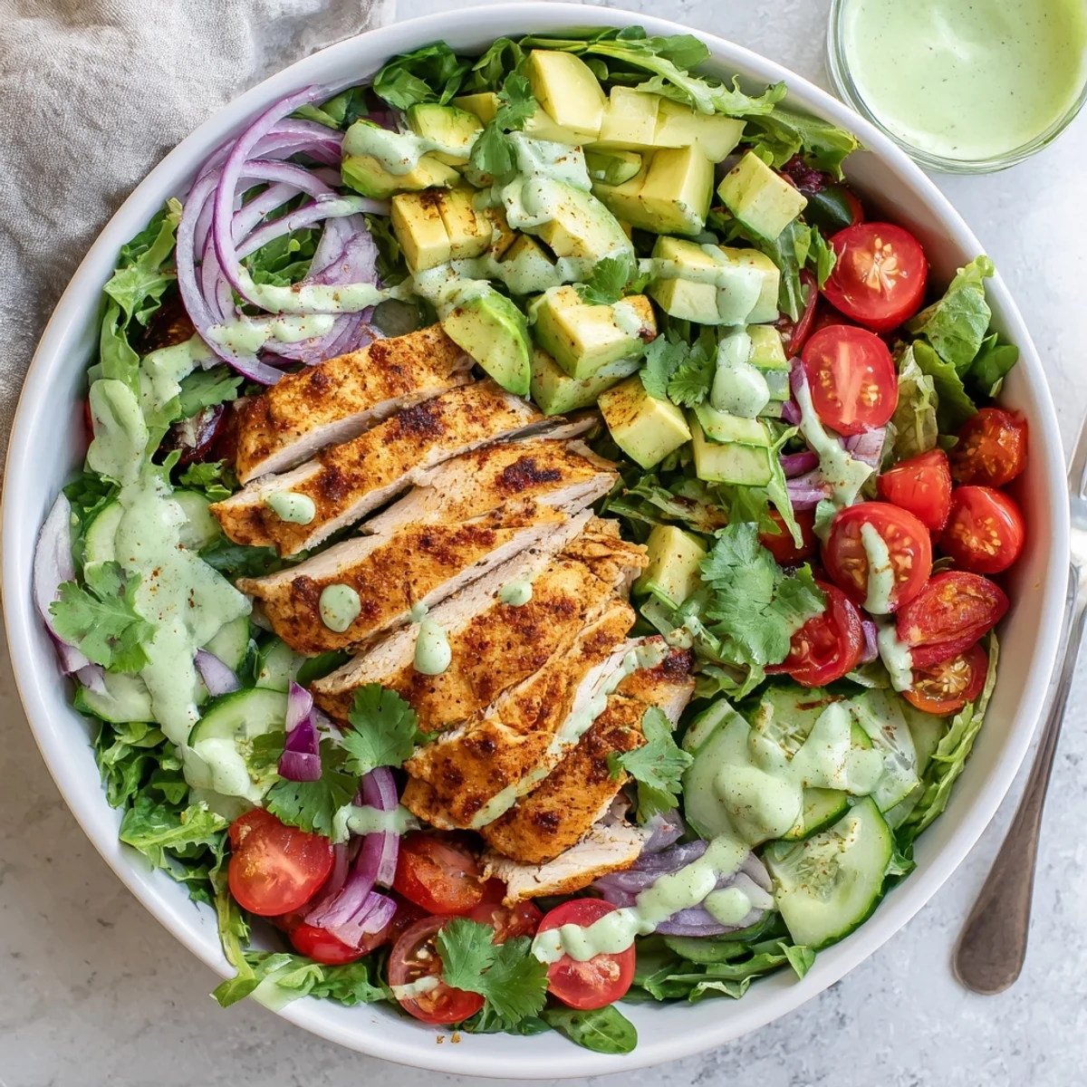 Healthy gluten-free salad bowl featuring grilled spiced chicken, ripe diced avocado, crisp vegetables, and tangy green dressing drizzled on top