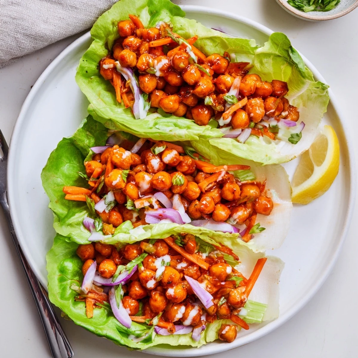 Zesty Buffalo Chickpea Lettuce Wraps with crunchy celery, carrots, and lemon wedge