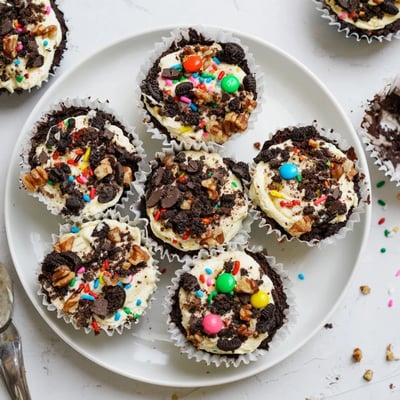 Individual loaded brownie cheesecake cups with crushed Oreos and pecans on white plate