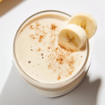Thick protein-rich Greek yogurt banana smoothie poured into a clear glass with straw