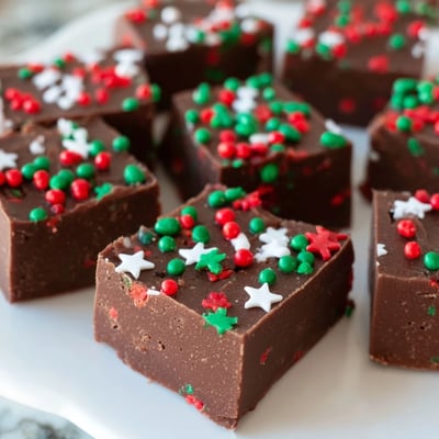 Rich chocolate Christmas fudge with sprinkles glistening under soft holiday kitchen lighting